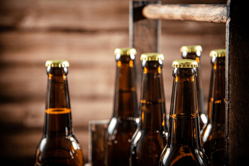 Close-up of brown glass beer bottles with gold caps arranged in a vintage wooden carrier box.