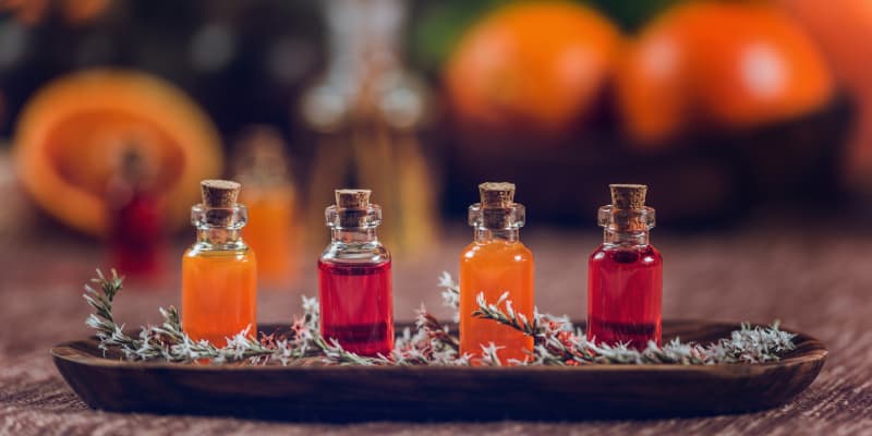 Four small glass vials filled with orange and red liquid elixirs arranged on a wooden tray with dried herbs.