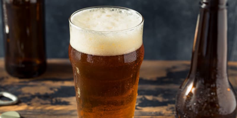 A cold glass of non-alcoholic German amber beer with a thick white foam head and condensation, sitting on a rustic wooden table.