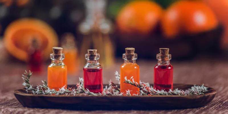 Four small glass vials filled with orange and red liquid elixirs arranged on a wooden tray with dried herbs.