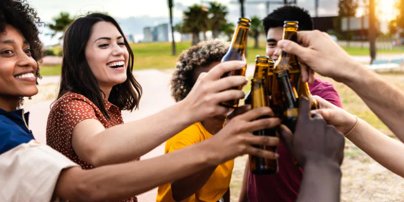 An overhead view of a diverse group of five happy friends sitting around a wooden table, clinking large glass mugs of golden beer in a celebratory toast.