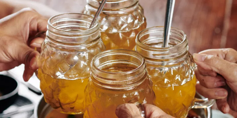 A group of friends clinking textured glass mugs filled with golden, effervescent kombucha over a dinner table.