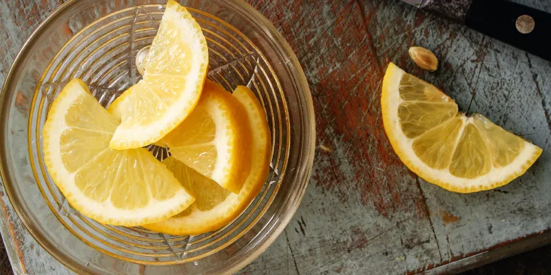 Fresh lemon slices in a glass bowl next to a knife on a rustic wooden cutting board.