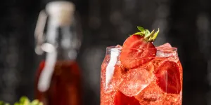 A tall, refreshing red drink filled with ice and fresh strawberry slices, highlighting the final strawberry syrup result.